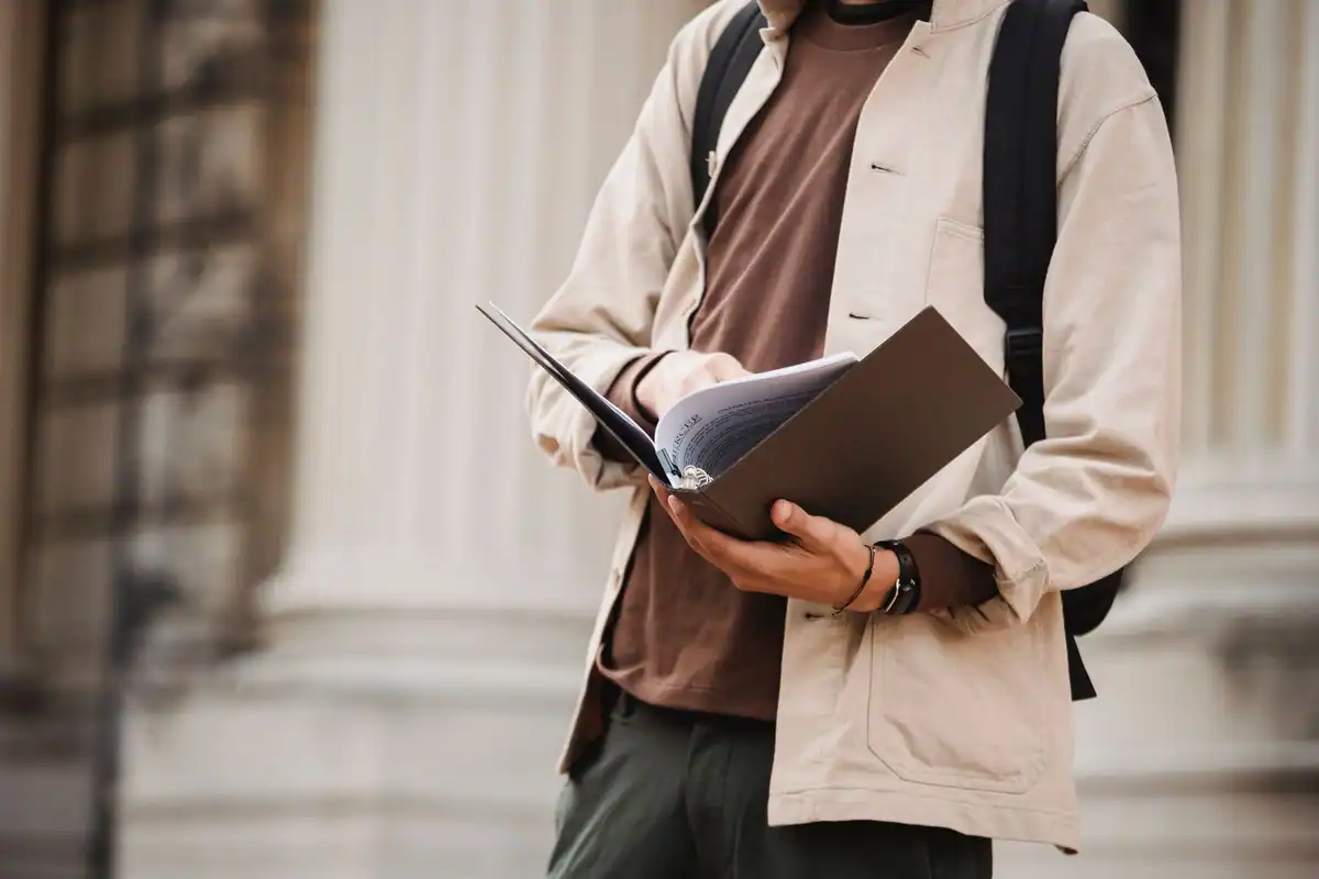 Tânăr cu dosarul de acte în mână lângă coloanele clădirii universității