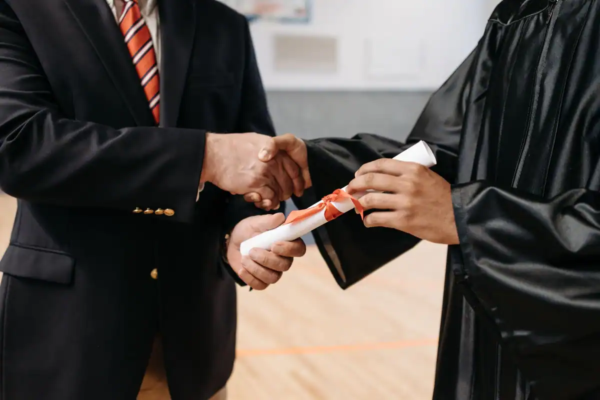 Absolvent care primește diploma și o strângere de mână de la reprezentantul finanțatorului