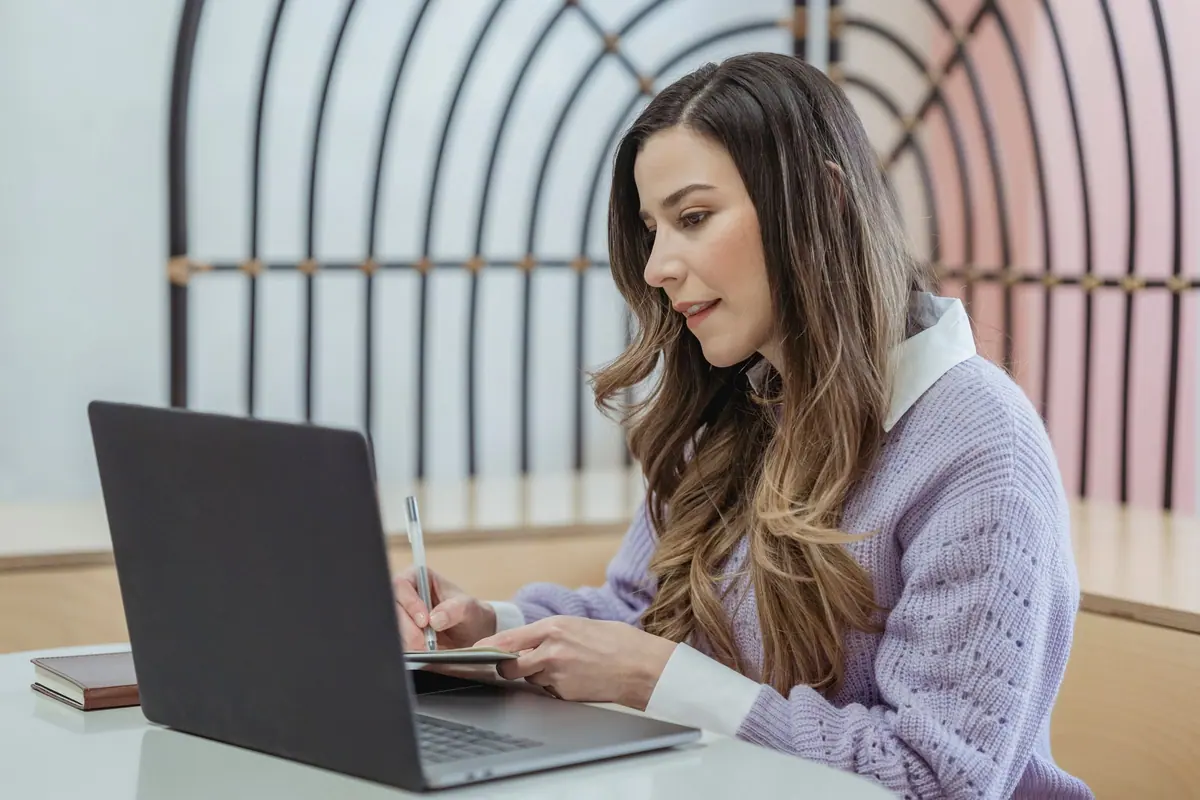 Tânără care își redactează dosarul de bursă la laptop, cu agenda deschisă