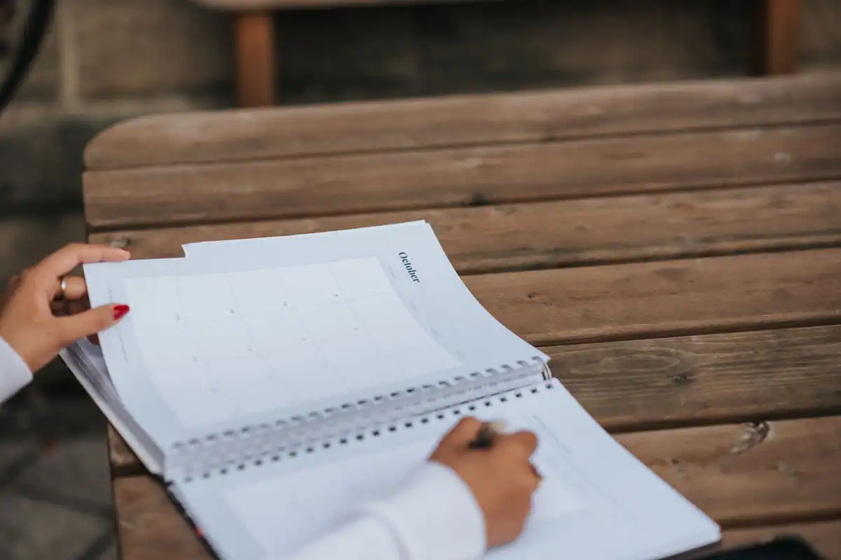 Studentă care își notează creditele și examenele în agendă, la o masă în parc