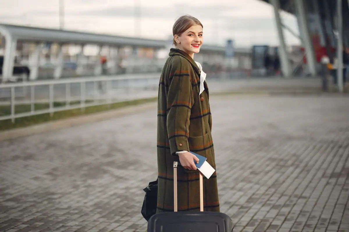 Studentă zâmbitoare cu bagaj și pașaport în terminalul aeroportului înainte de mobilitate