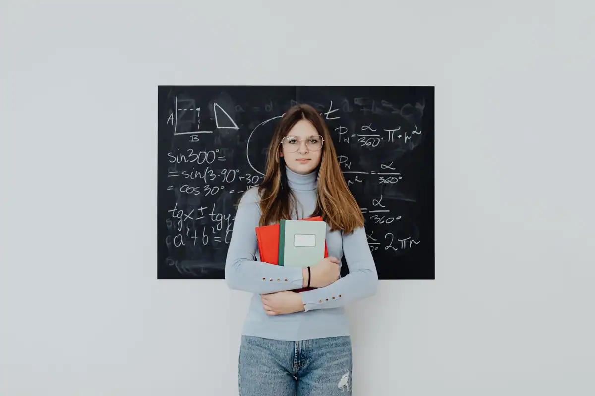 Elevă de gimnaziu cu ochelari în fața tablei cu exerciții de matematică