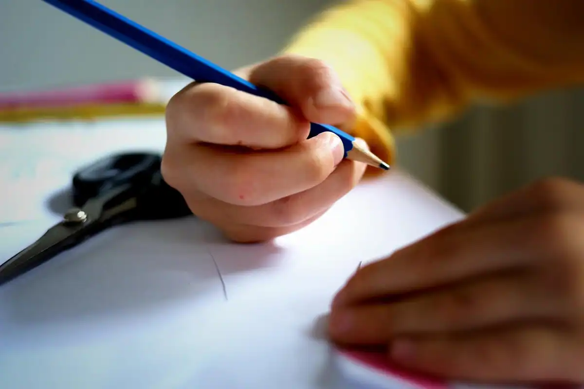 Mână de elev care scrie atent cu creionul pe foaia de lucru