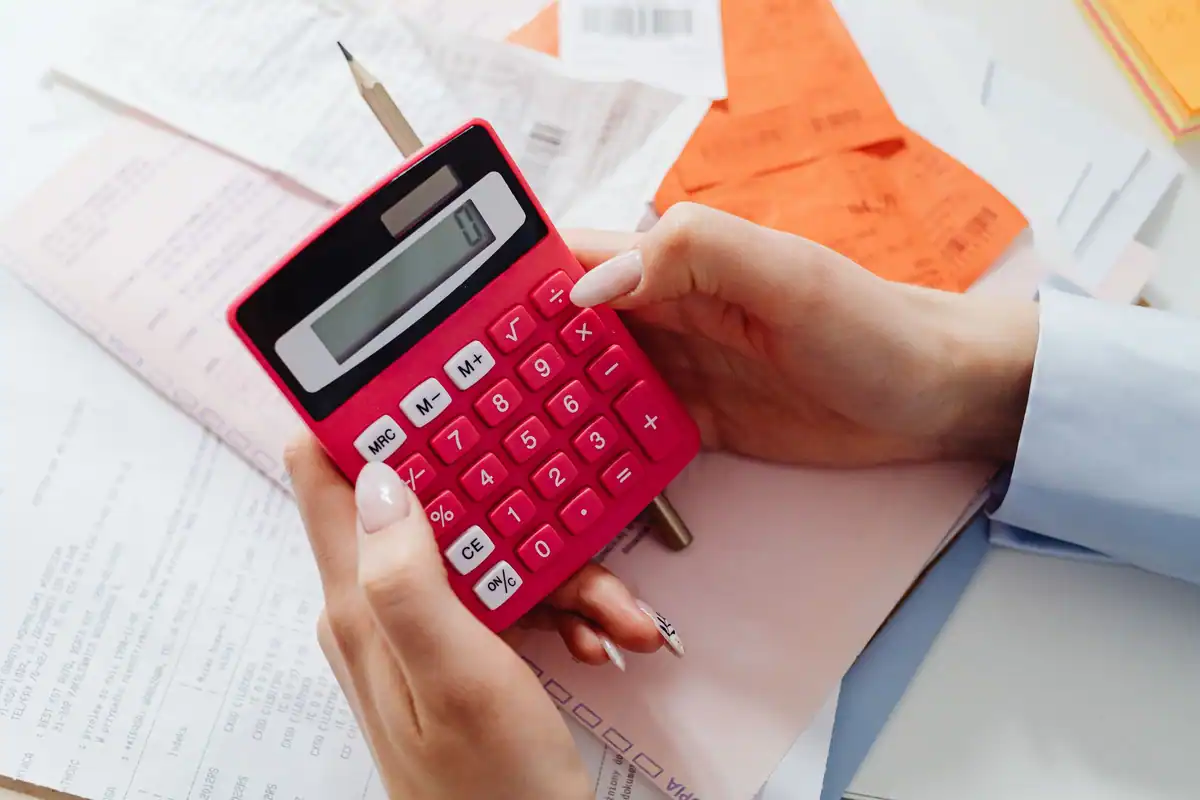 Mâini care țin un calculator roșu deasupra chitanțelor pentru taxa de studii