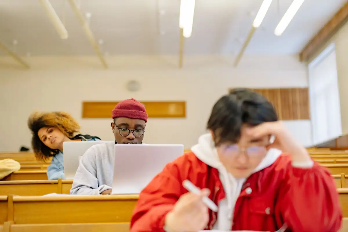 Studenți în amfiteatru care își iau notițe pe caiet și laptop în timpul cursului