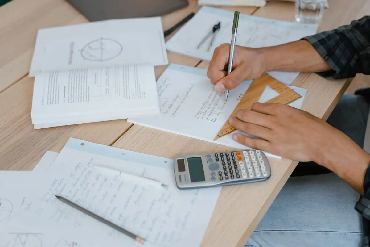 Elev care calculează media cu un calculator și foi de exerciții pe birou