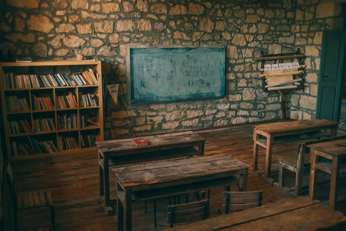 Sală de clasă rustică, cu pereți de piatră, bănci de lemn și tablă