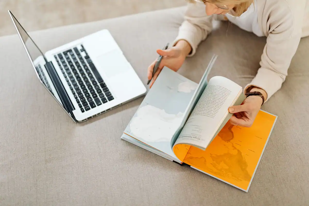 Tânără care caută informații despre universități pe laptop și într-un atlas