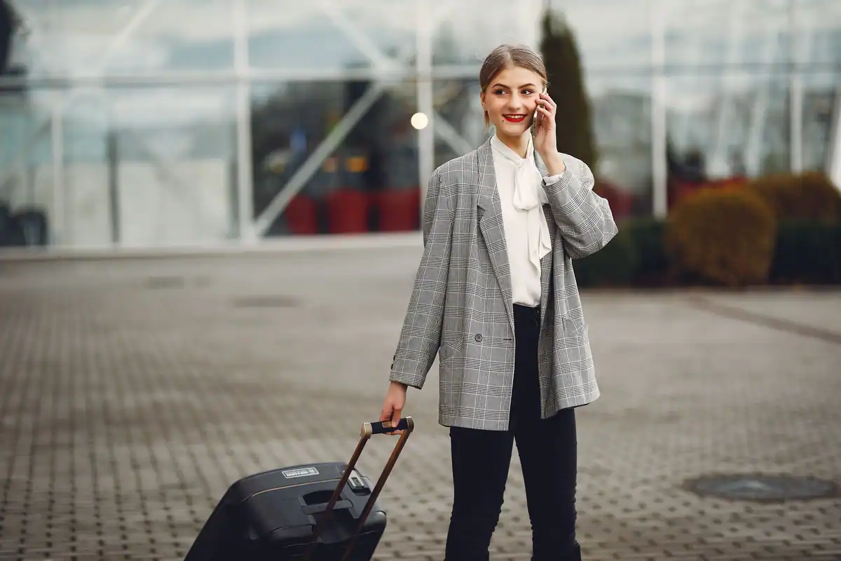 Tânără cu valiza la aeroport, care vorbește la telefon înainte de plecarea la studii
