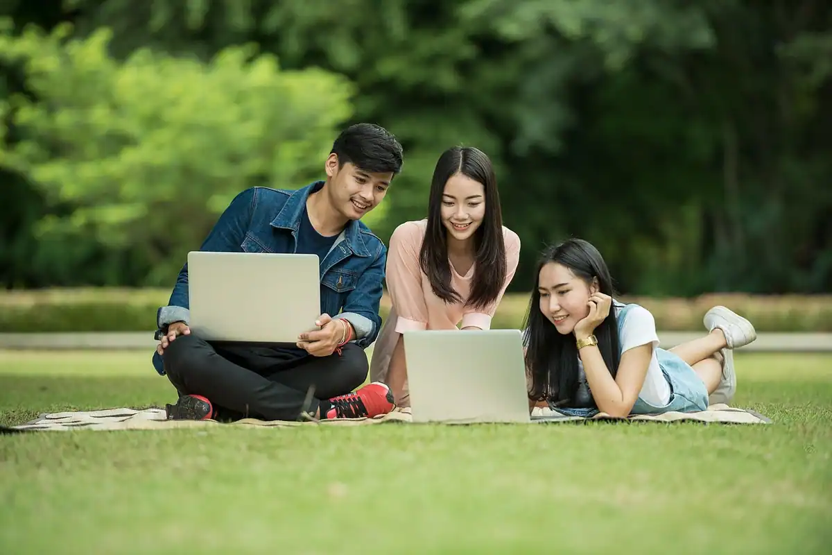 Trei studenți cu laptopuri în parc, care își explică unul altuia lecția