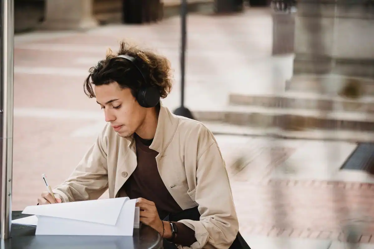 Tânăr cu căști care scrie pe o foaie exercițiile pentru testul de limbă